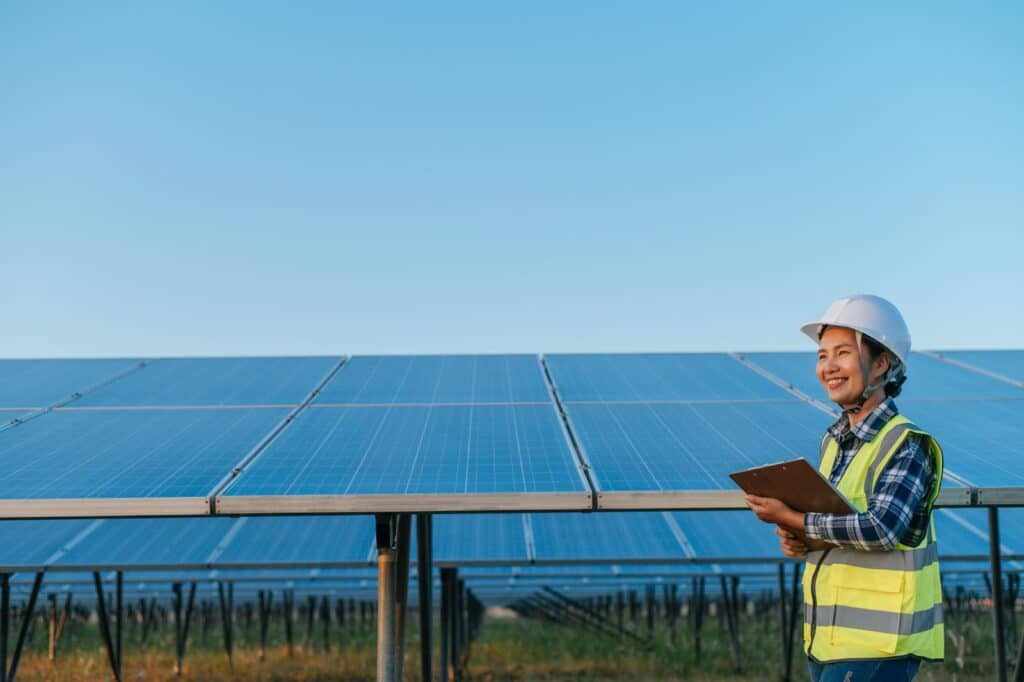 solar development with female worker  with safety uniform holding clipboard standing in front of panels